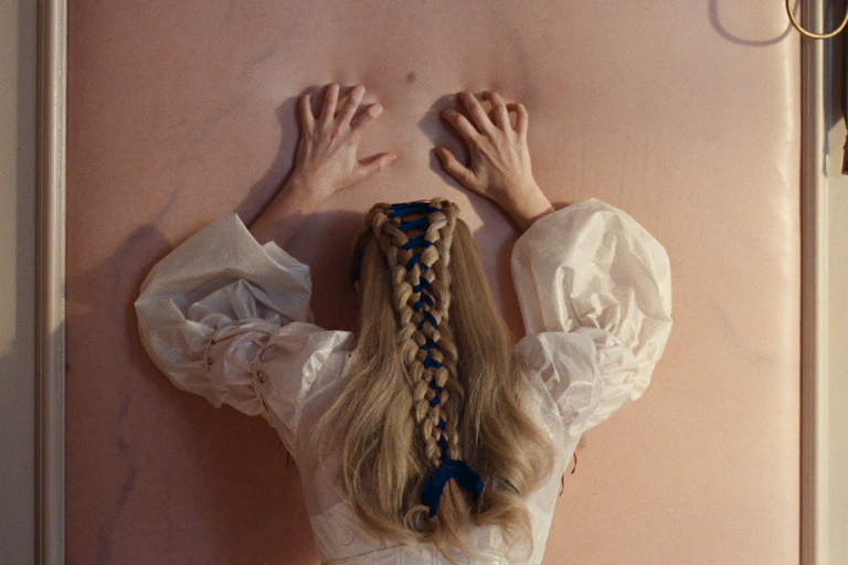 Margot Robbie leaning against a wall in anguish, the wall looks like it is made of her skin
