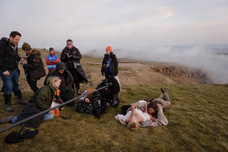 Jacob Elordi and Margot Robbie in an embrace on the ground outside, while being filmed for Wuthering Heights