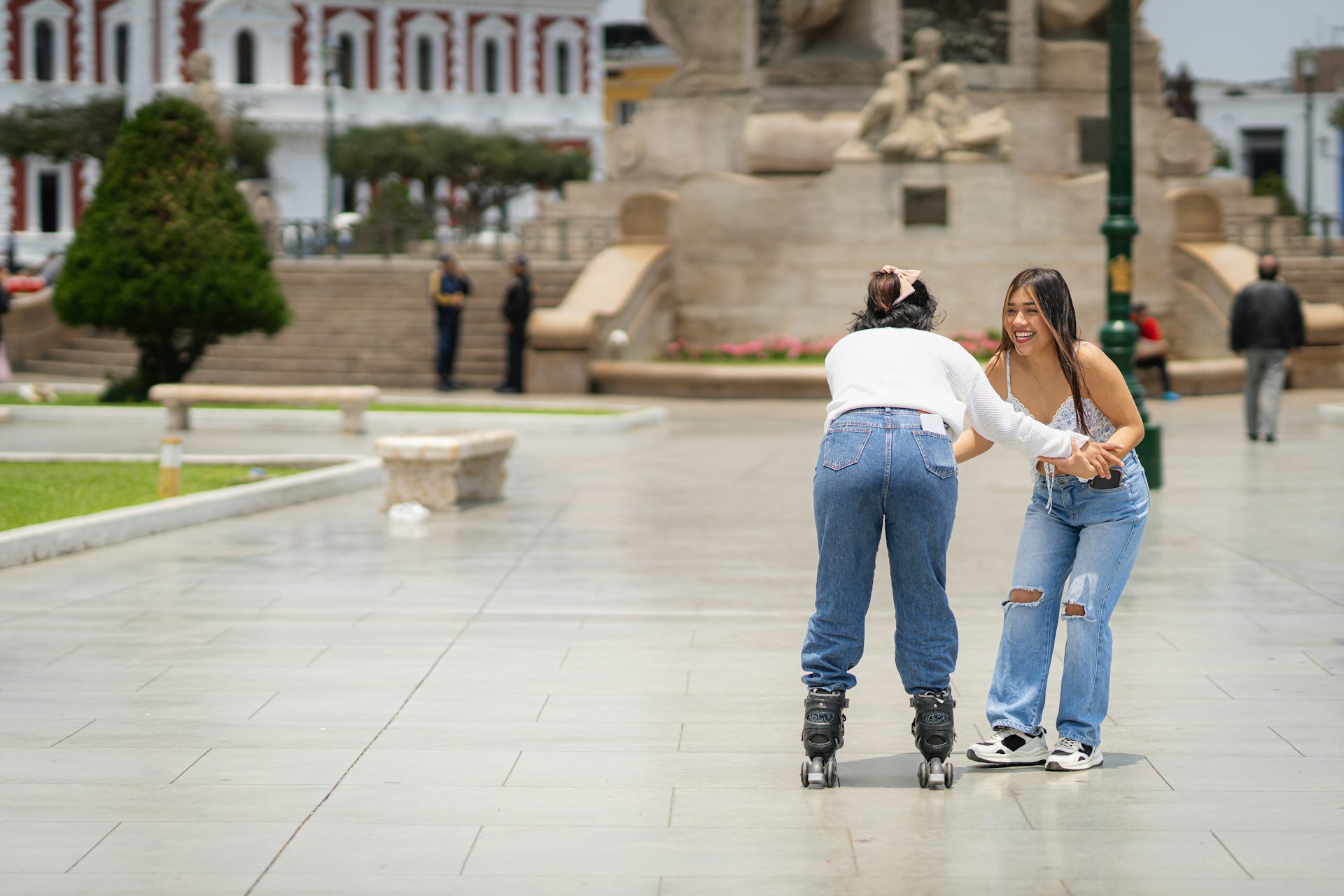 Dues adolescents patinen al carrer agafades de les dues mans.