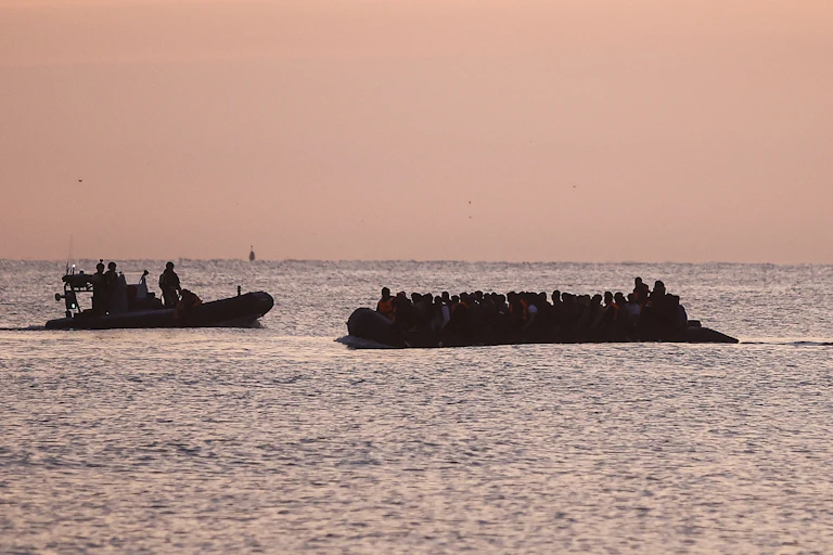 Silhouette of a small boat full of people in the Channel at dusk