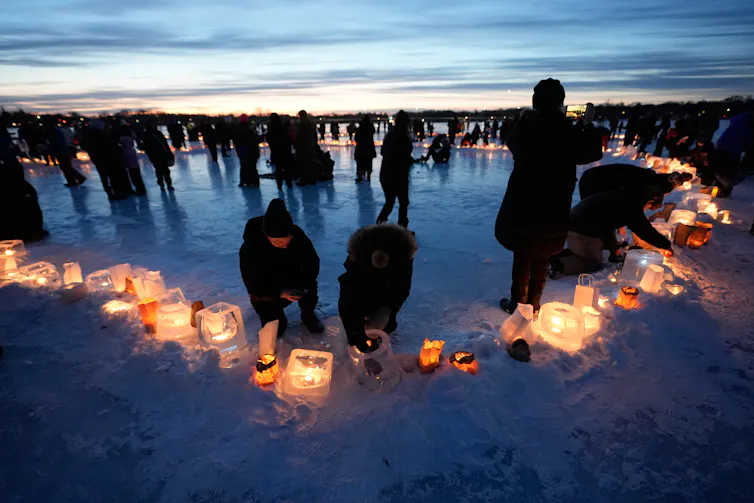 People stand on a frozen lake at dusk lighting candles.