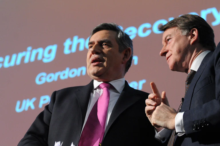 gordon brown and peter mandelson standing in front of a red background with the words securing the economy.