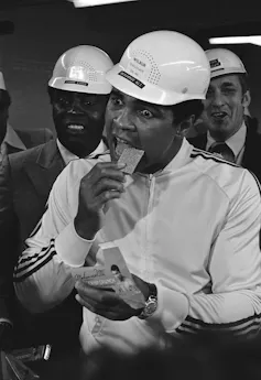 El hombre del sombrero de construcción blanco le da un gran mordisco a la barra de chocolate.