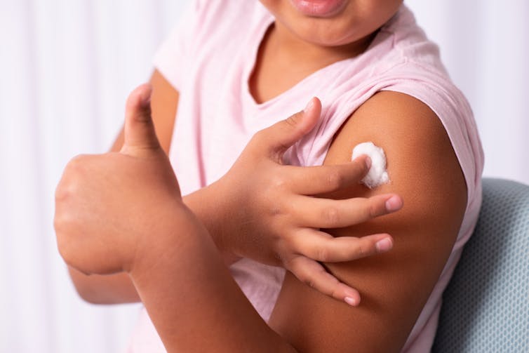 A child holds a cotton ball against their upper arm, where they received a vaccine