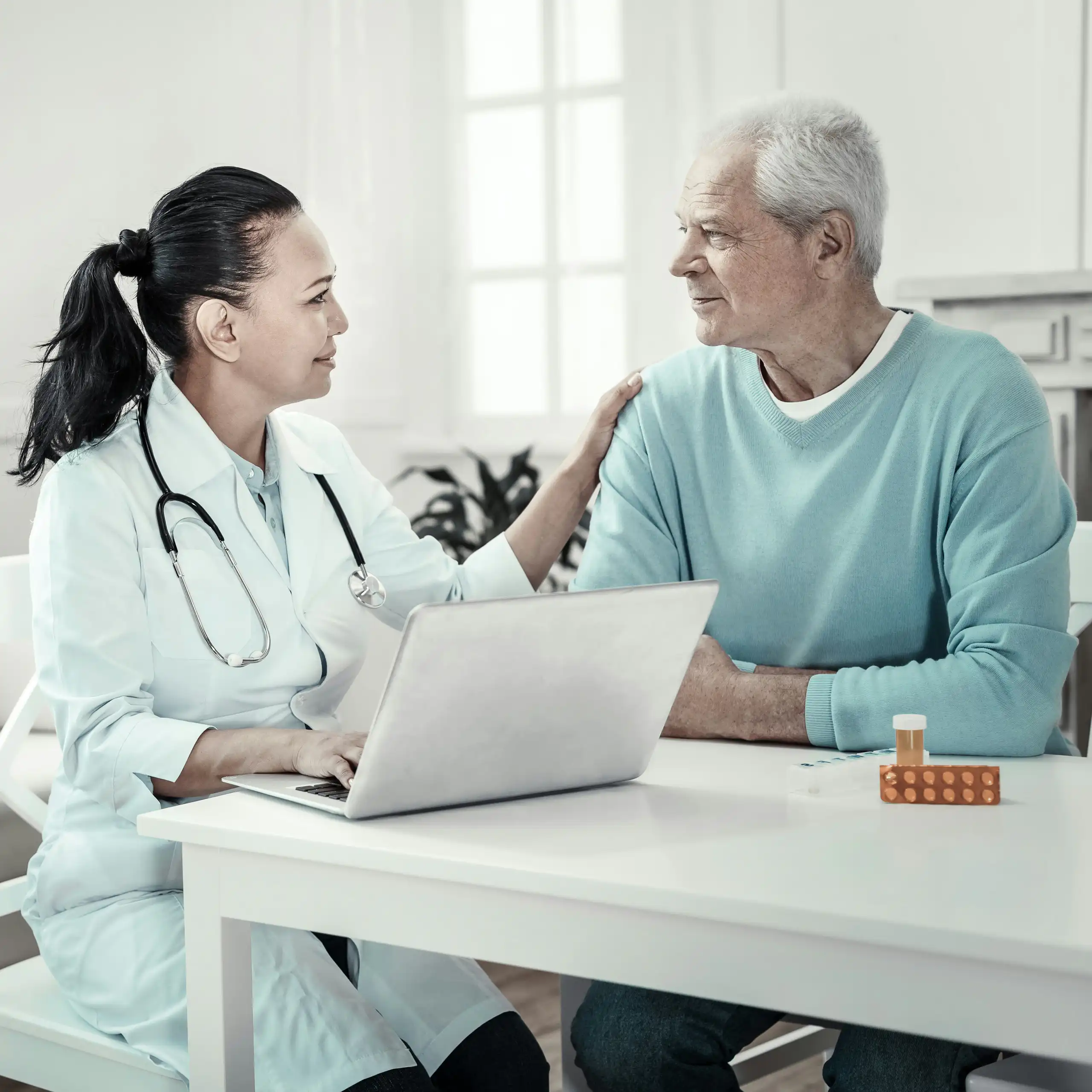 A man with grey hair with a health-care worker in a white coat with a stethoscope