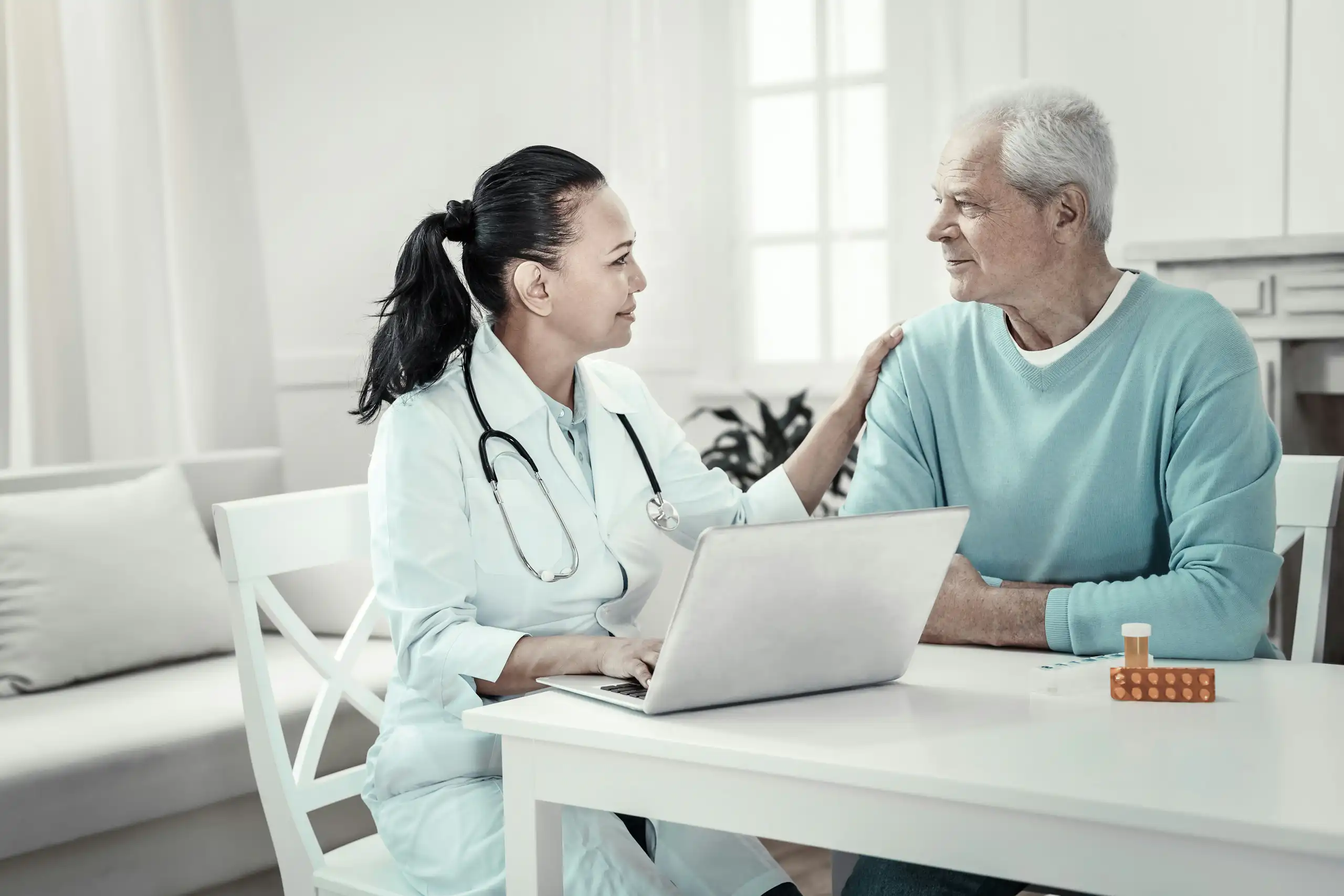 A man with grey hair with a health-care worker in a white coat with a stethoscope