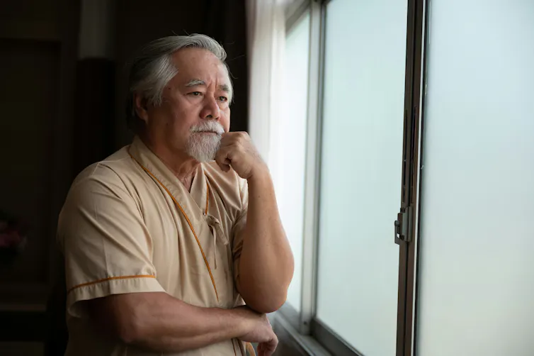A man with grey hair and a grey beard looking pensively out a window