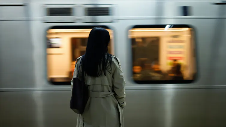 A woman in a trench coat stands on a train platform as a train pulls in