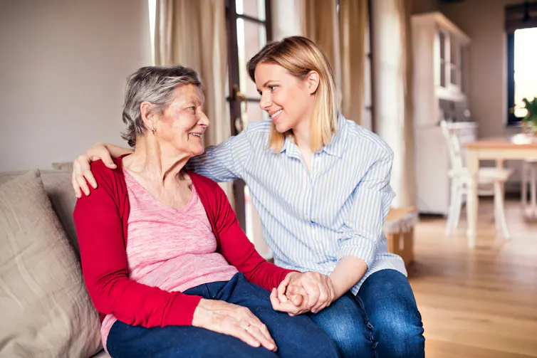 An younger woman sitting on a sofa with her arm around an older woman