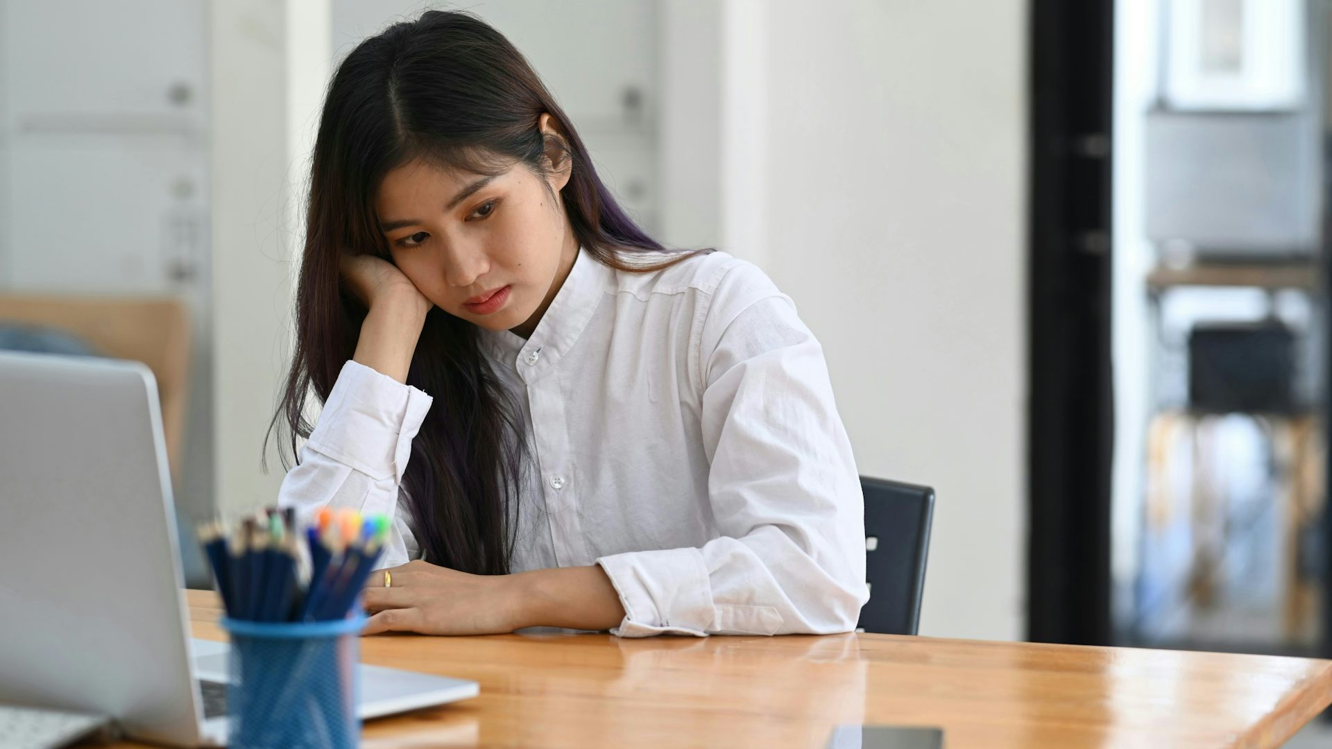 Una mujer joven está sentada en una mesa, apoyando su mejilla en su mano.