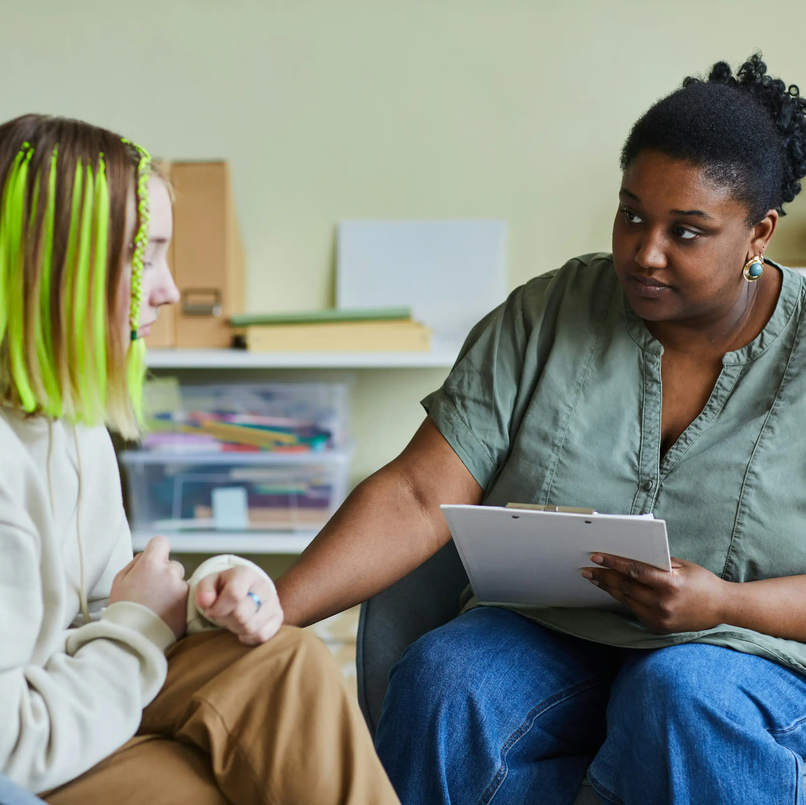 A woman holding a clipboard and looking sympathetically at another woman and holding her hand