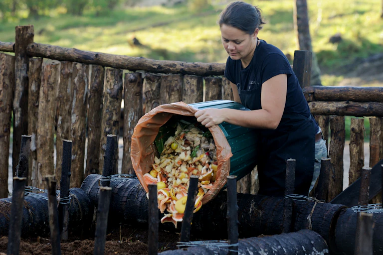 A woman tips scraps into a compost heap.