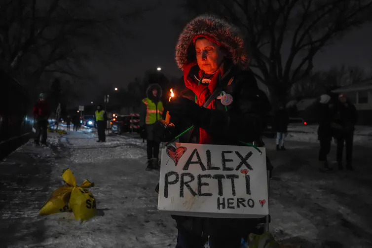 A woman attends a vigil at night, with a sign remembering ICE shooting victim Alex Pretti.
