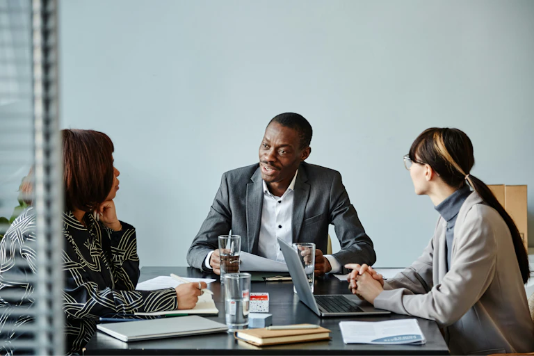 Two women seated at a table with a man look at him as he speaks