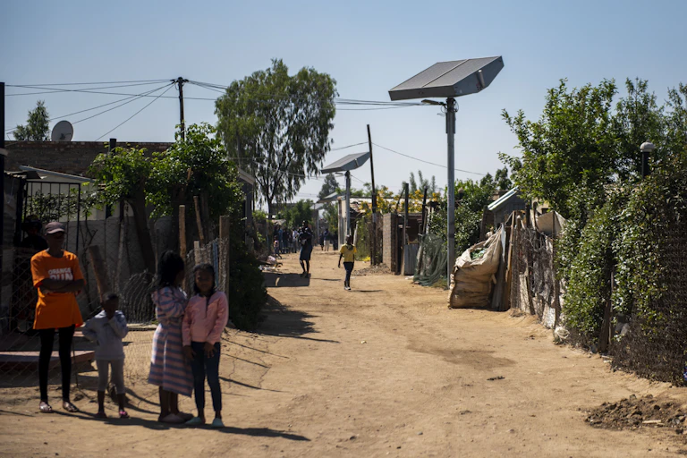 A line of corrugated iron shacks with a pole between them on which is mounted a giant solar panel