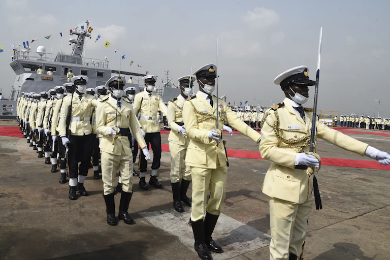 People marching in uniform, a ship in the background