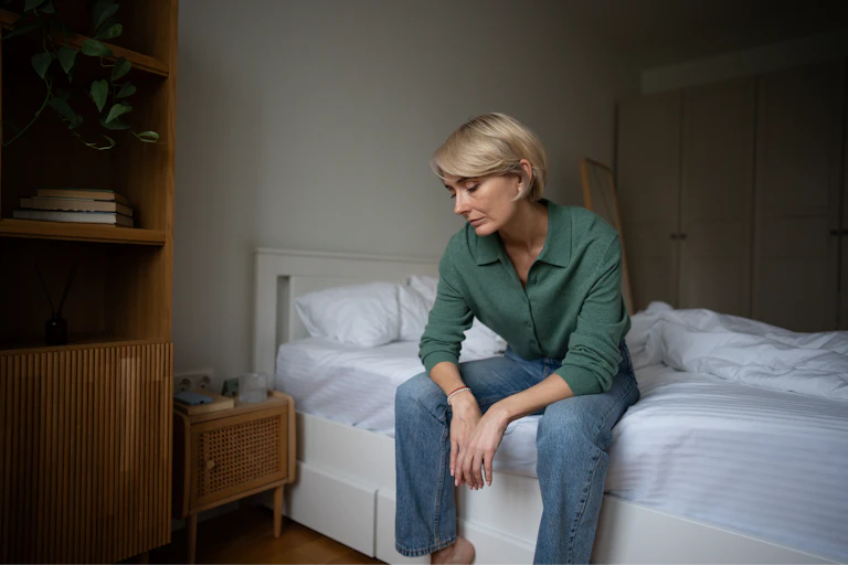 Tired looking woman sitting on the edge of a bed.