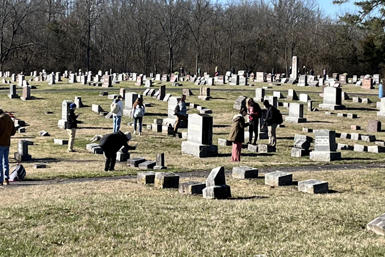People scattered throughout a cemetery, taking photos and notes of headstones