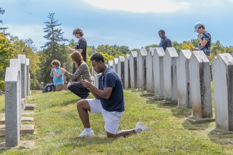 People kneeling, crouching and standing before rows of headstones, taking images and notes