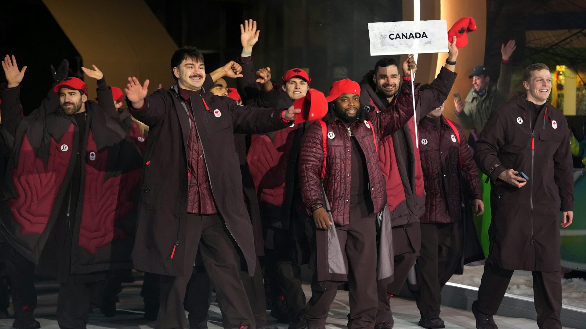 Un grupo de personas con chaquetas granates caminan detrás de alguien con el cartel Canadá.