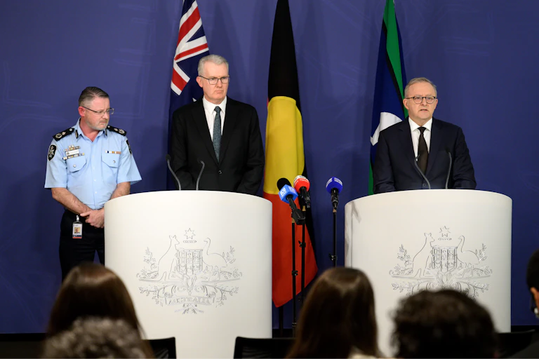 Two men in suits and a police officer stand behind lecterns to speak about terrorism