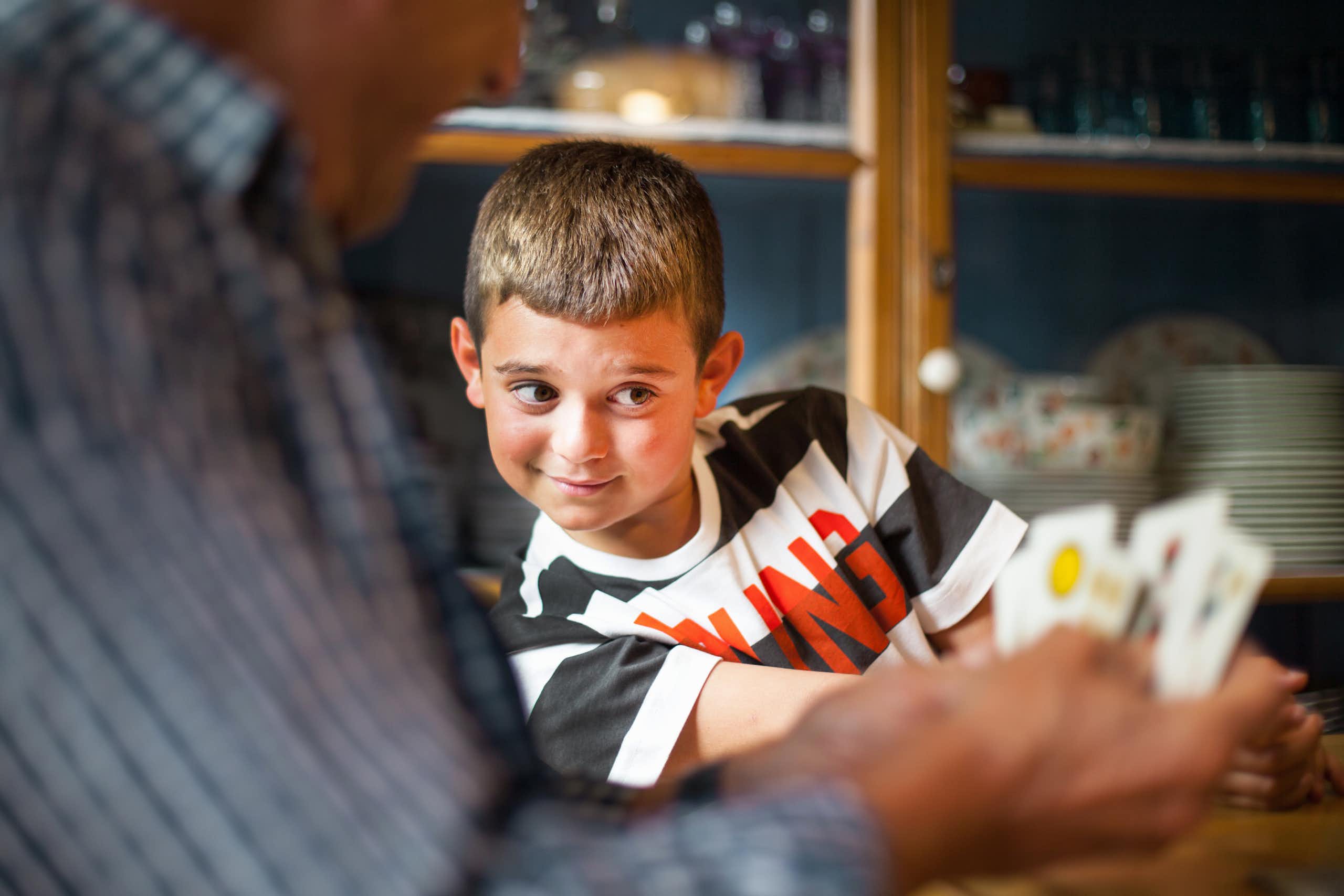A young boy tries to peek at the cards of the adult sitting next to him.