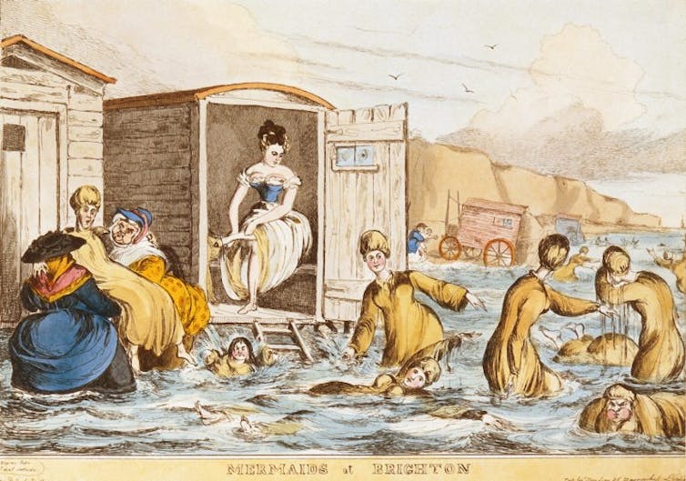 An old engraving shows women swimming in the ocean behind wooden bathing machines.