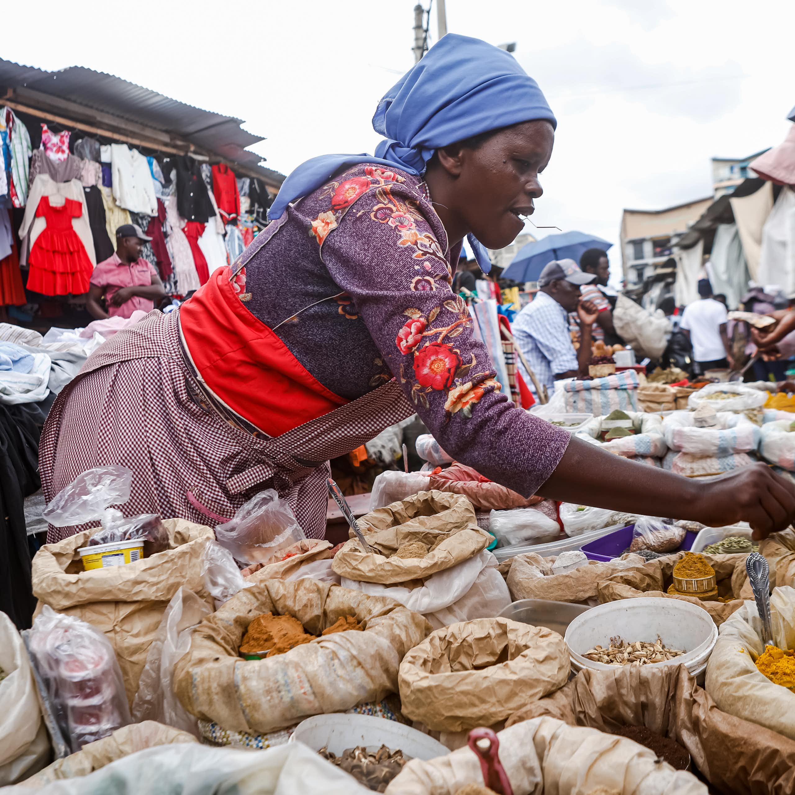 A woman leaning over bags of spices at an open market