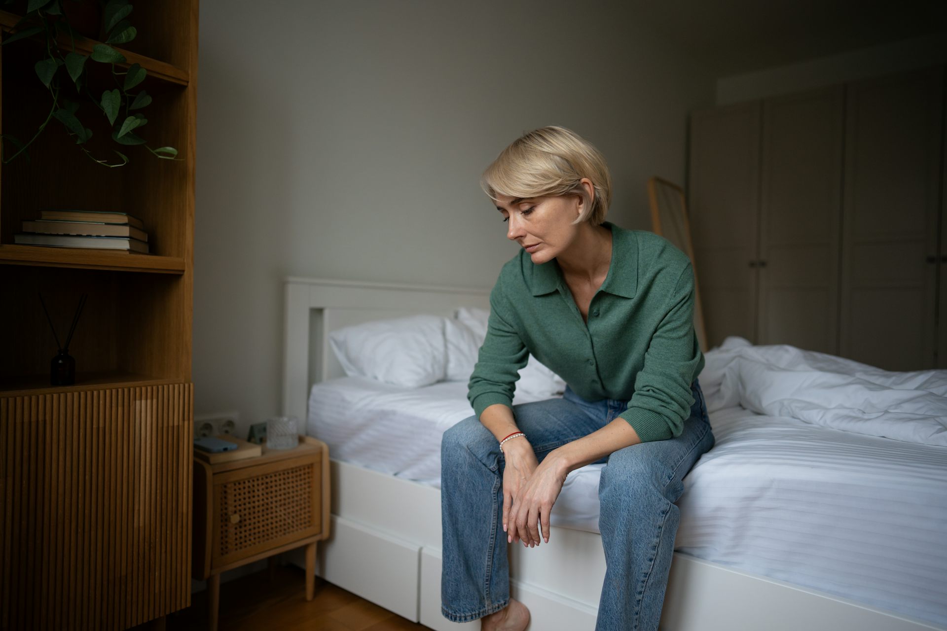 Tired looking woman sitting on the edge of a bed.