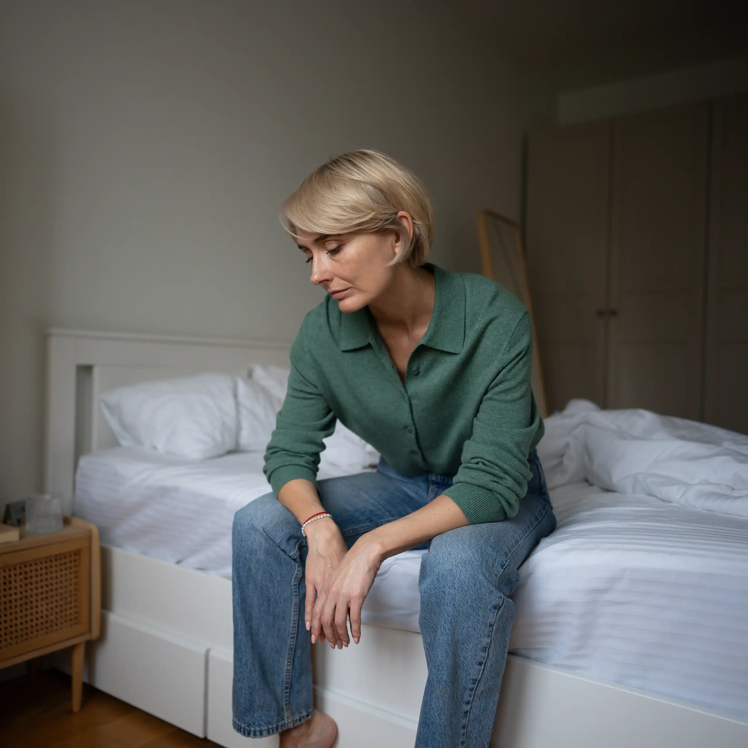 Tired looking woman sitting on the edge of a bed.