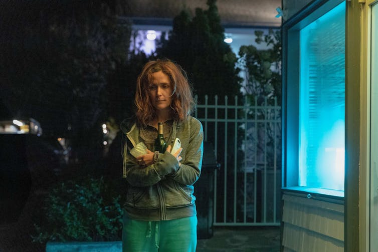 Lo que 'Si tuviera piernas te patearía' nos dice sobre la maternidad y el sacrificio ingrato 2 Una mujer camina en la oscuridad sosteniendo botellas de vino.