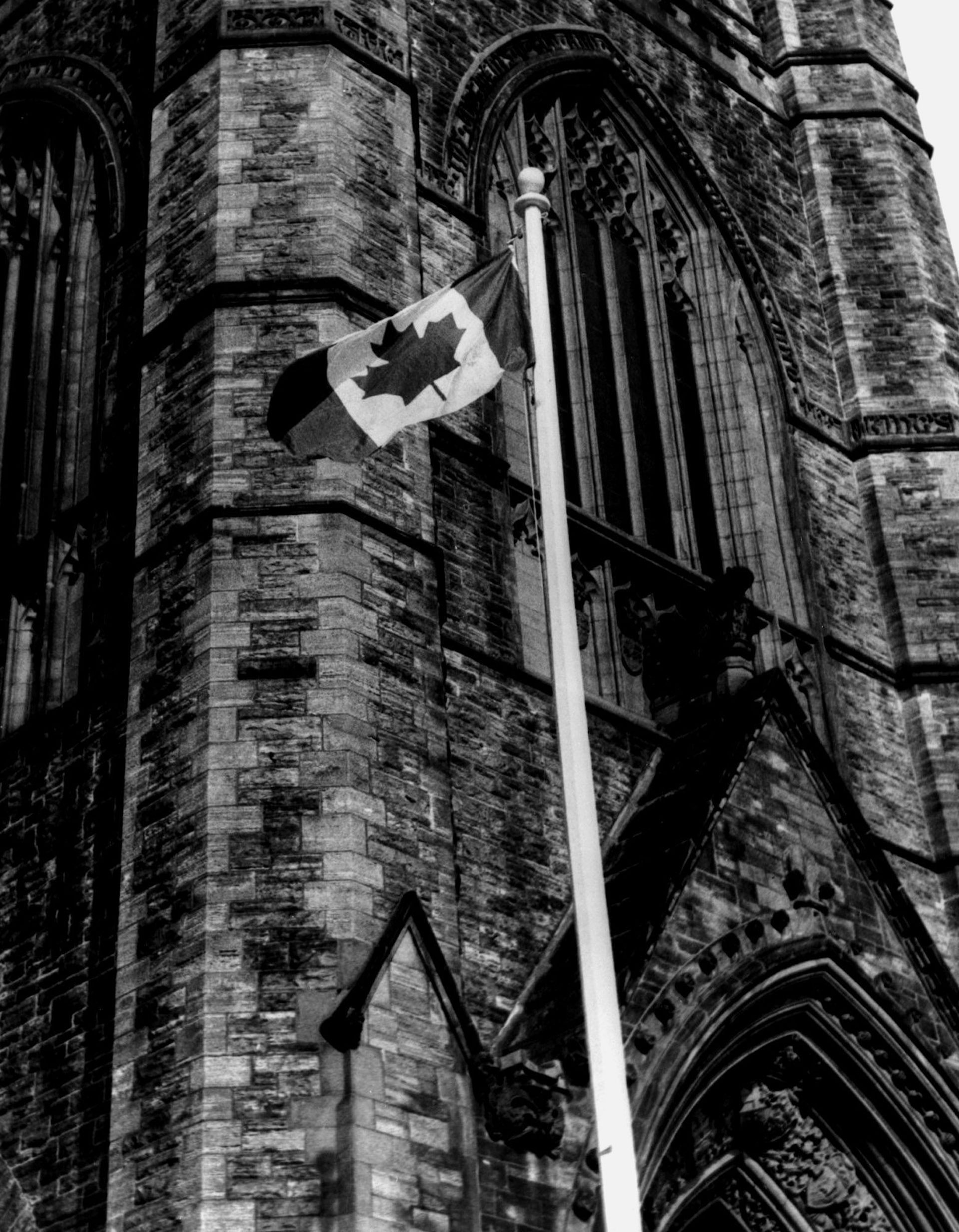 Una fotografía en blanco y negro muestra la bandera canadiense ondeando frente a la Torre de la Paz.