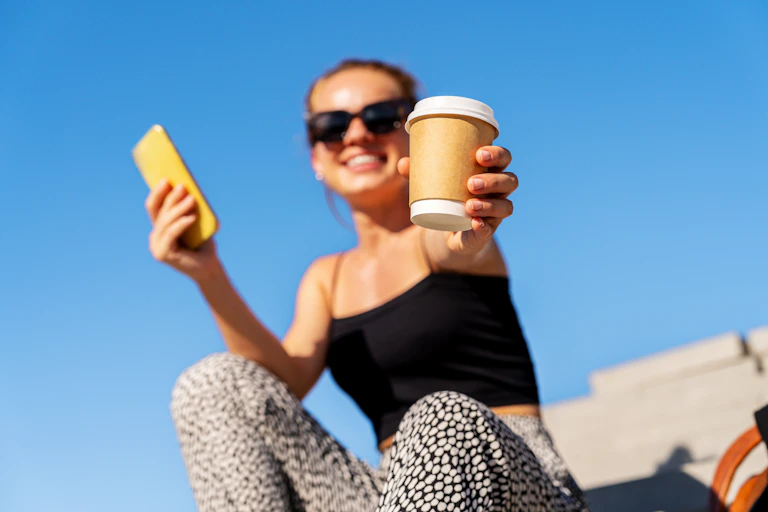 Woman passing a cup of takeaway coffee to someone.