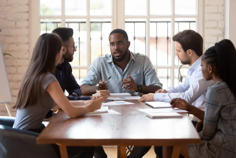 group of five professionals sitting around a table talking