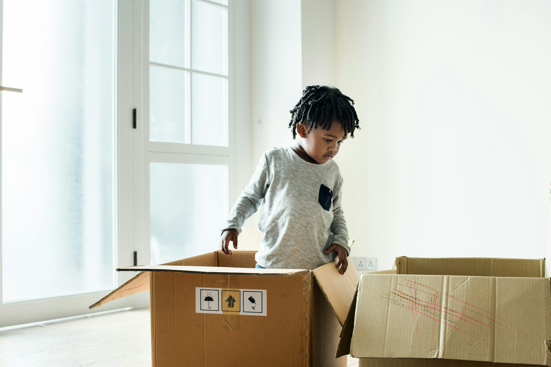 A boy stands in thought with some cardboard boxes. 