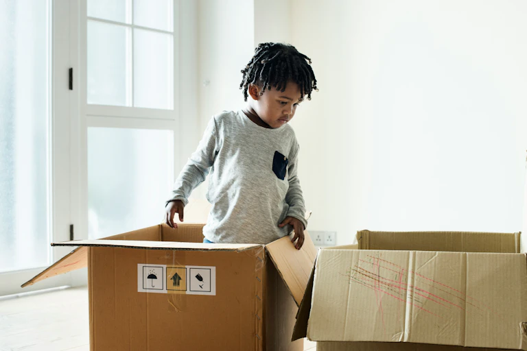 A boy stands in thought with some cardboard boxes.
