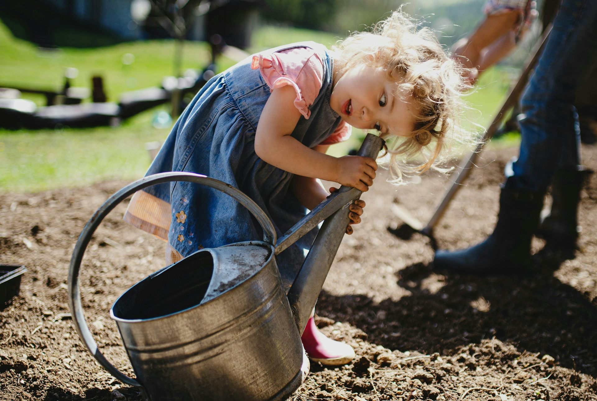 A child has her ear on the spout of a watering can.