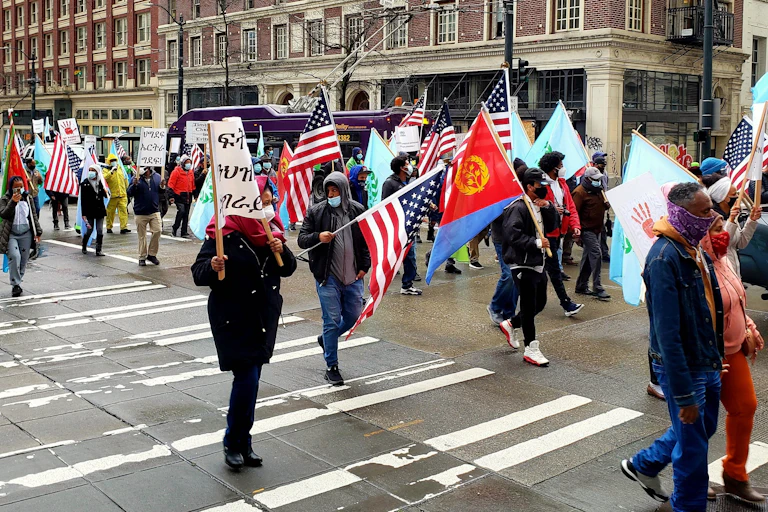 A group of people walking while holding up flags in front of buildings