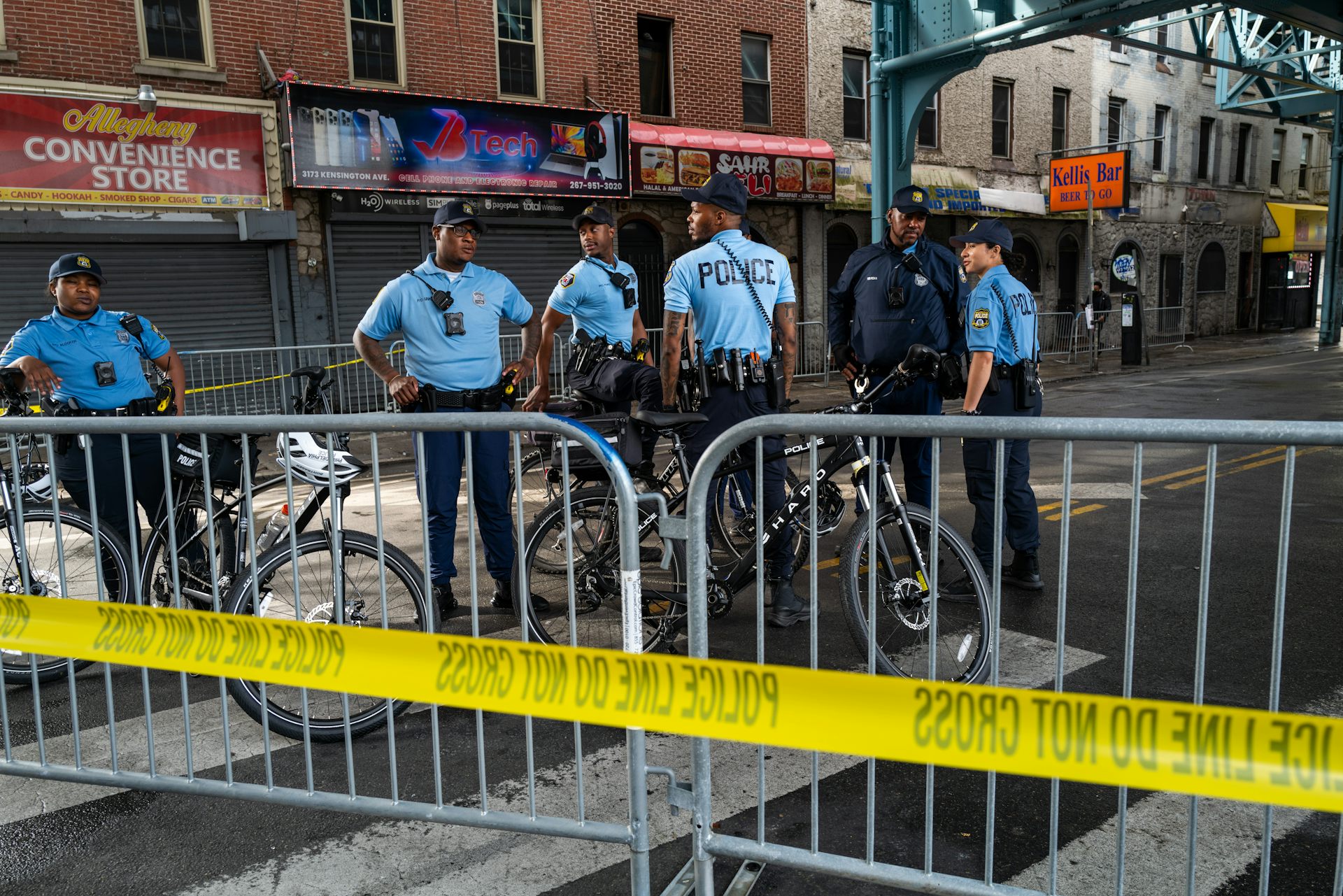 A group of uniformed police stand on an empty commercial street behind metal gate and yellow police tape