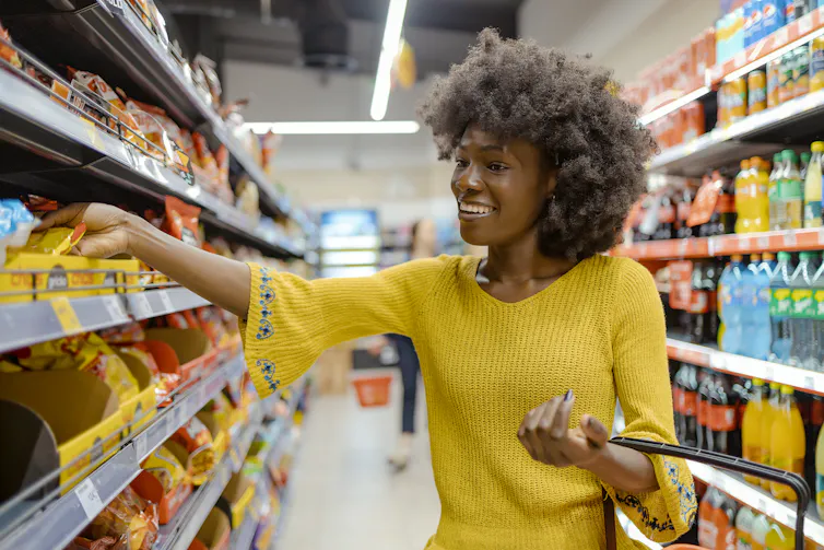 smiling woman in grocery aisle reaches for a candy