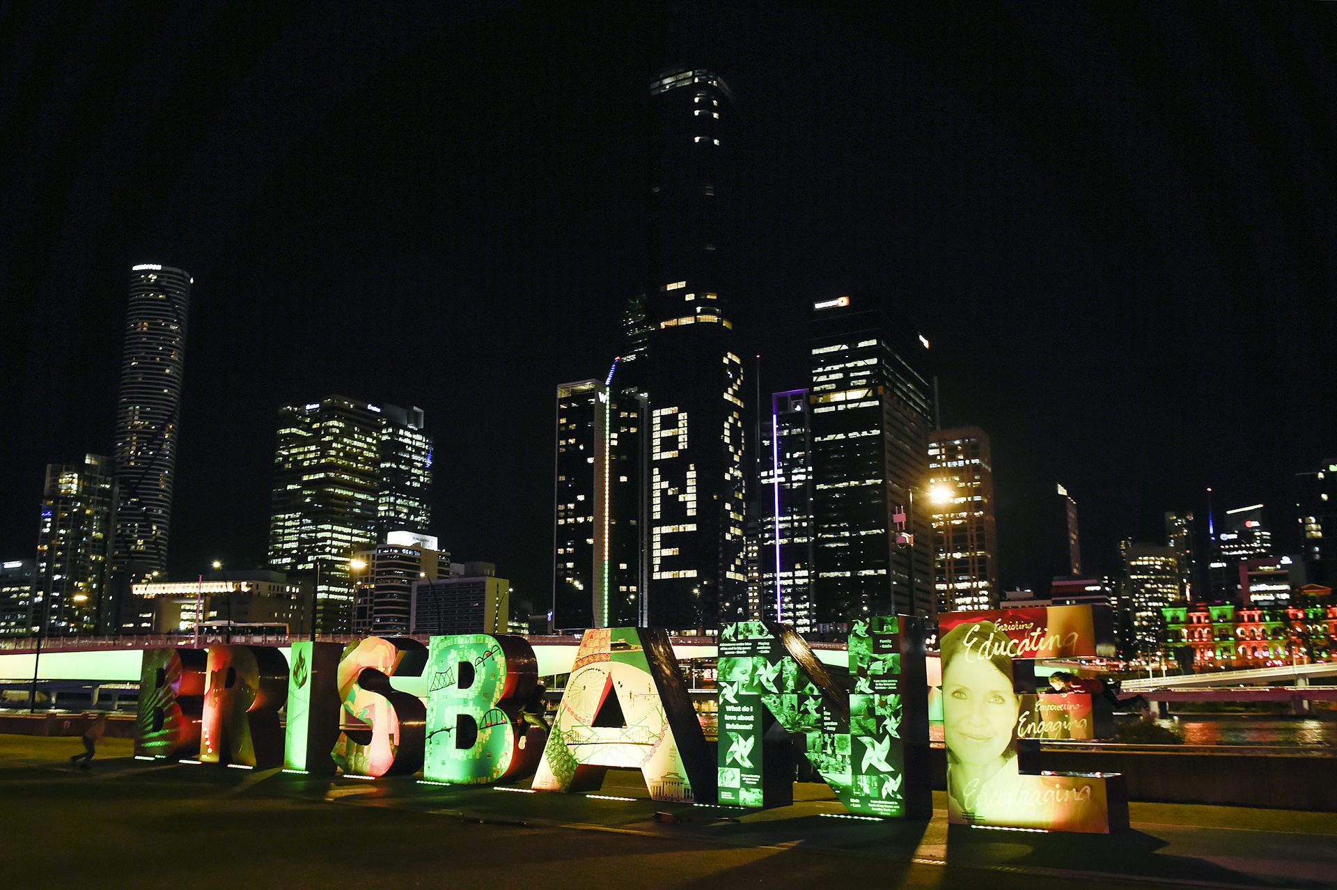 A close up of the Brisbane sign on the city's South Bank waterfront, with the city skyline lit up with BNE 2032 in the background