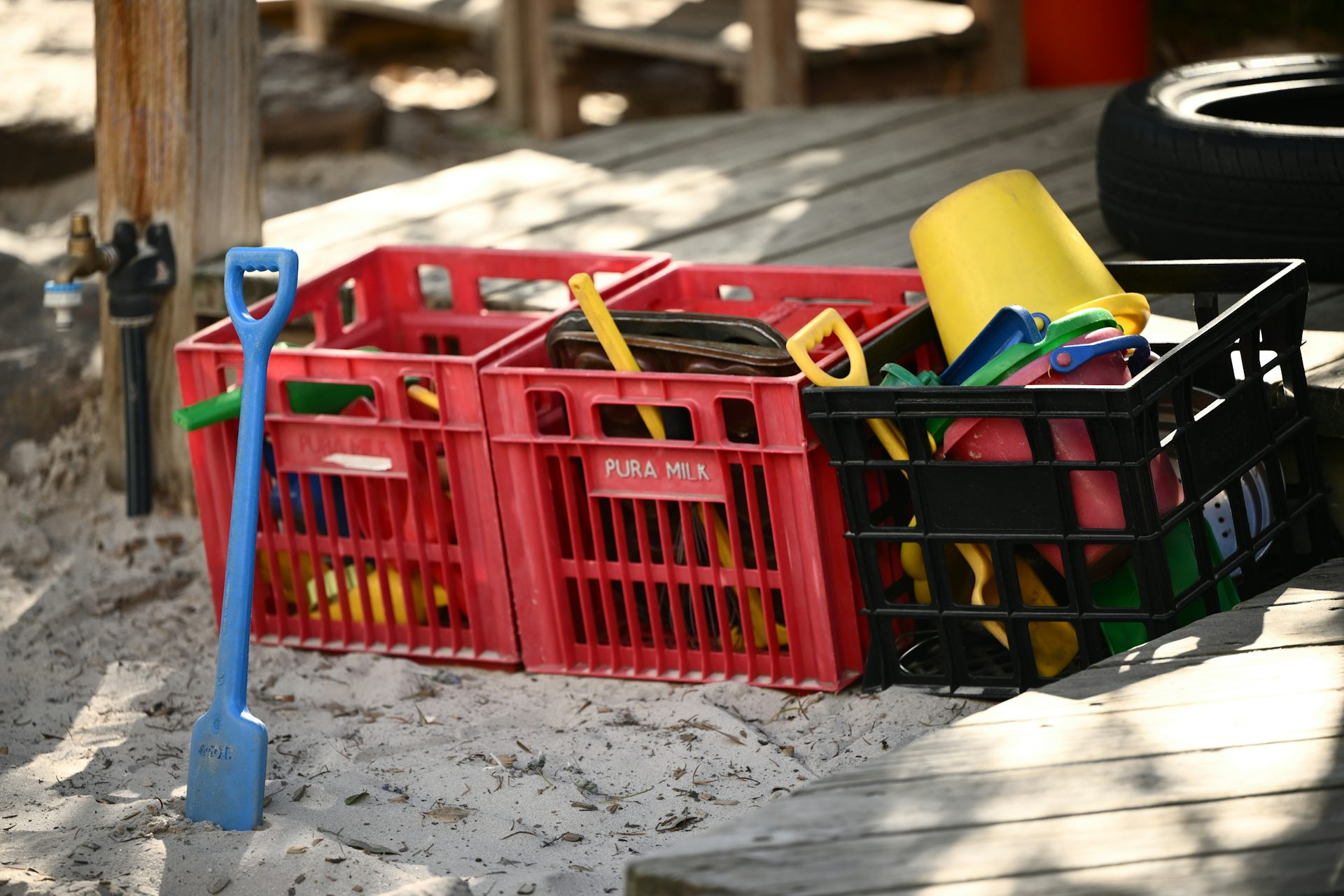 Buckets and spades stored in milk crates, next to a sand pit. 