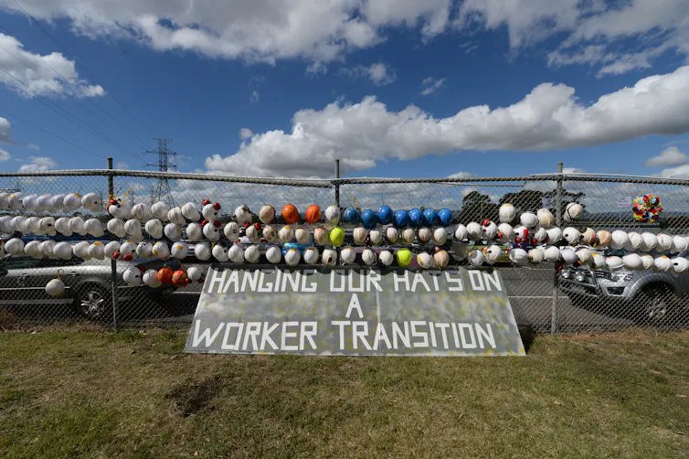 A line of worker helmets hands on a fence outside the Hazelwood power station after it is closed.