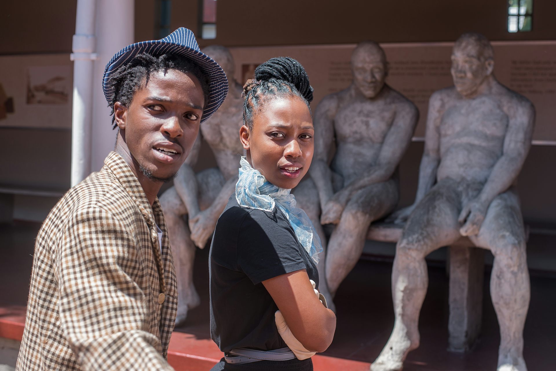 Two young people in front of a sculpture of seated people