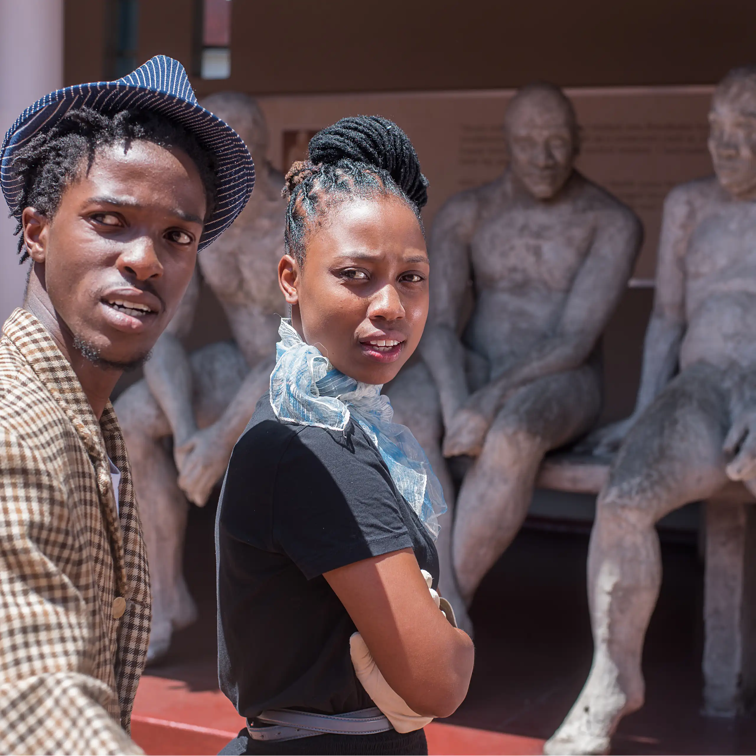 Two young people in front of a sculpture of seated people