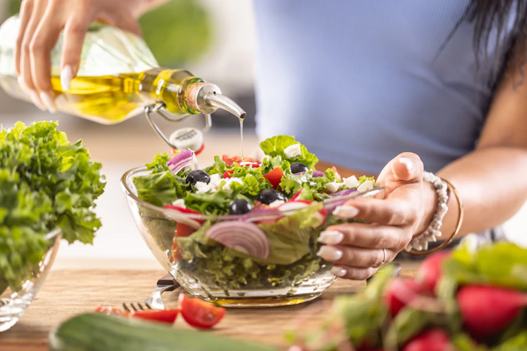 A woman pours olive oil onto a salad.