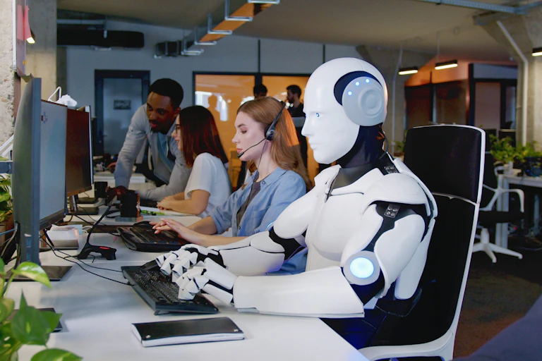 Humanoid robot working at desk with human colleagues.