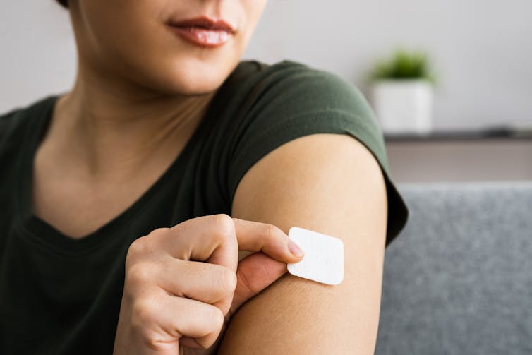 A woman places a hormone treatment patch on her arm.