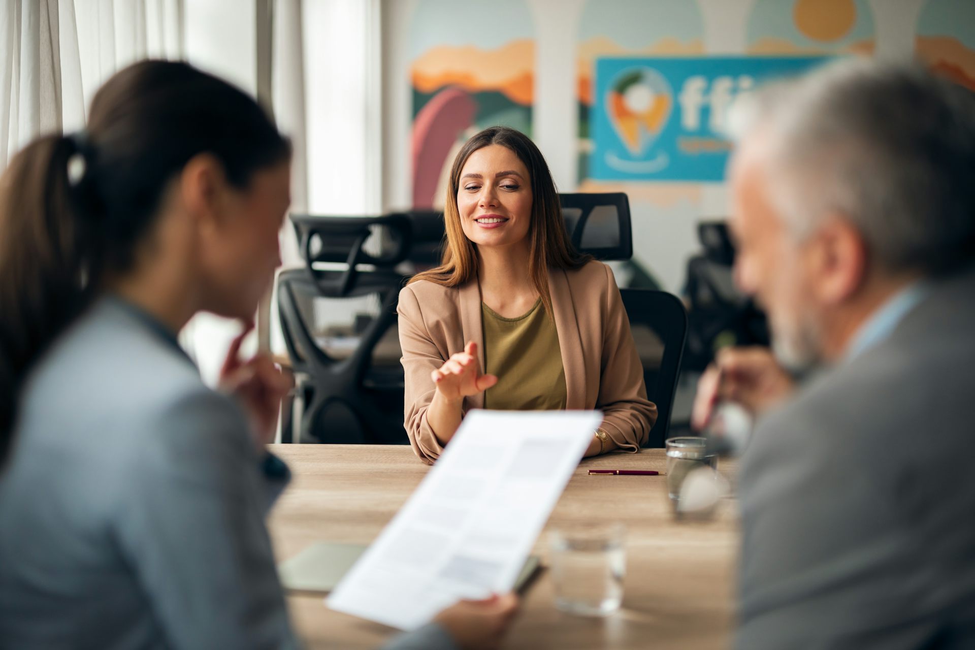 Woman across desk from two people holding a paper document.