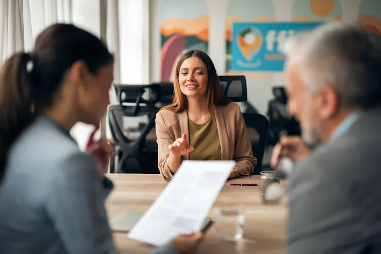 Woman across desk from two people holding a paper document.